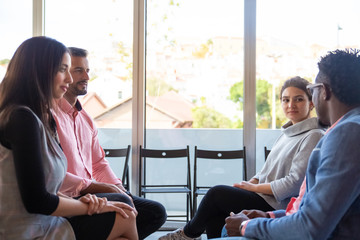 Cheerful co-workers sitting on chairs and talking. Smiling colleagues discussing some questions....