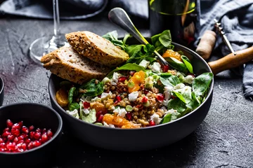Foto op Aluminium Buckwheat salad with lamb's lettuce, pomegranat seeds, goat cheese, mandarine and spring onion, Served with whole grain baguette and red wine. Black table and black background. © mateuszsiuta
