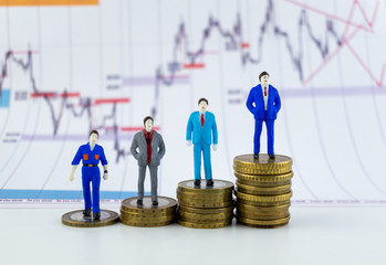 Miniature people: small businessmen and a worker standing on stack of coins with some coins laying behind them on a chart backround. Money, Financial, Business Growth concept.
