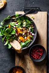 Poster Buckwheat salad with lamb's lettuce, pomegranat seeds, goat cheese, mandarine and spring onion, Served with whole grain baguette and red wine. Black table and black background. © mateuszsiuta