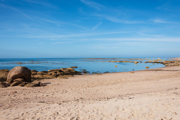 Fototapeta na wymiar Manche, Normandy, France. Beautiful sandy beach with boulders in calm water. People relaxing at background. Sailing and fishing mooring in bay near natural breakwater. Summer eco tourism in Europe.