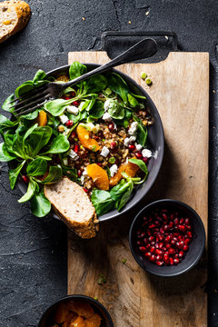 Buckwheat Salad With Lamb's Lettuce, Pomegranat Seeds, Goat Cheese, Mandarine And Spring Onion, Served With Whole Grain Baguette And Red Wine. Black Table And Black Background.