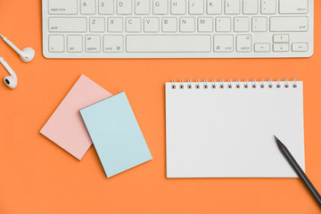 Blank spiral notebook, keyboard, pencil and supplies on orange background. Top view with copy space for input the text.