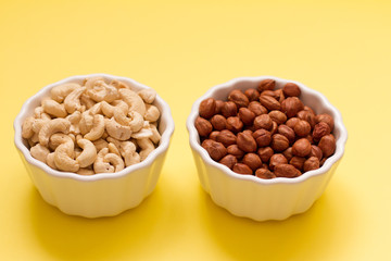 hazelnuts and walnuts in two white cups on a yellow background. lots of nuts. the concept of proper nutrition and health. Healthy food and snacks, organic vegetarian food. the view from the top. 