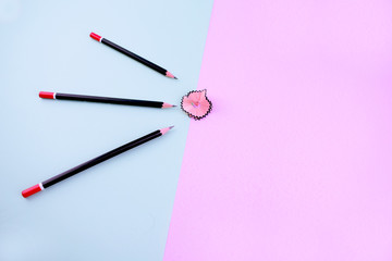 bunch of black sharpened pencils over a light blue background point at a pencil shaving which is over a pink background
