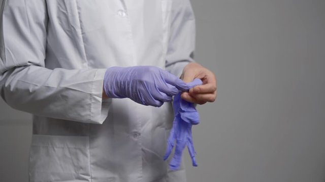 A medical worker in a white robe, wearing sewn gloves. The doctor or nurse complies with the standards of protection against viruses.