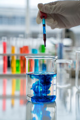 Scientist is dropping a liquid from pipette glass into a medical glassware.