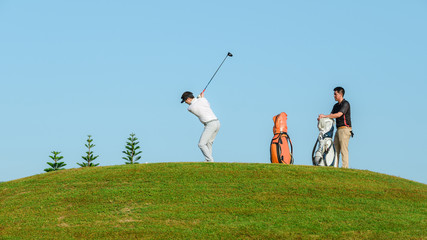 Two Male Golfers Walking Along Fairway Carrying Bags
