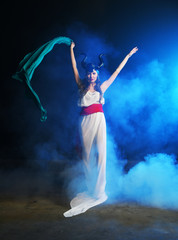 beautiful girl in the clothes of the goddess of the earth with a blue veil on a background of smoke