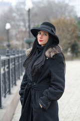 Fototapeta na wymiar A nice girl in a beautiful gray coat and hat walks in the park on a cold autumn / winter day. Portrait photography.