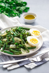 Fried wok green beans with egg, onions and spices in a white plate on a gray background. Flat lei. Top view.
