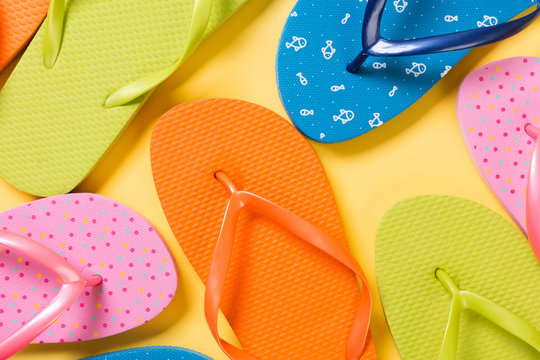 many colored flip flops on yellow background. Copy space top view