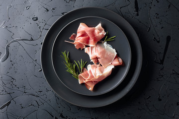 Prosciutto and rosemary on a black plate. Top view.
