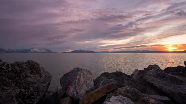 Time lapse of colorful sunset overlooking Utah Lake moving on slider past rocks.