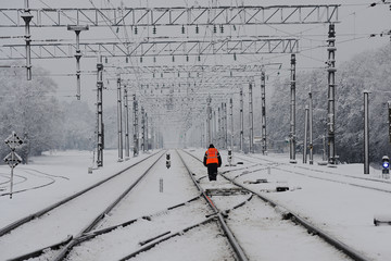 Electrified railway marked by snow leaving into the distance and a railway worker on the tracks