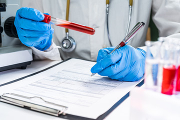 A doctor in a laboratory holds a test tube with a patient’s blood test. Concept - blood test for...