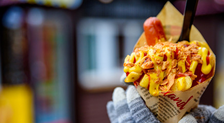 Young woman hands holding Belgian fried potatos with sausage, ketchup and sause, street fast food
