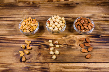 Various nuts (almond, cashew, hazelnut) in glass bowls on a wooden table. Vegetarian meal. Healthy eating concept