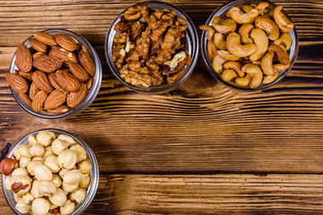 Various nuts (almond, cashew, hazelnut, walnut) in glass bowls on a wooden table. Vegetarian meal. Healthy eating concept. Top view