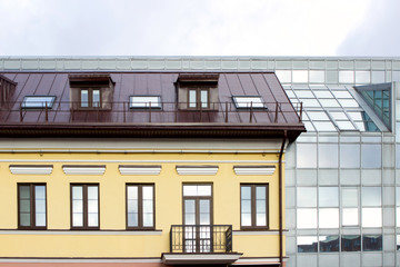 Fototapeta na wymiar old building and new modern glass building nearby. Yellow facade and metal forged balcony.
