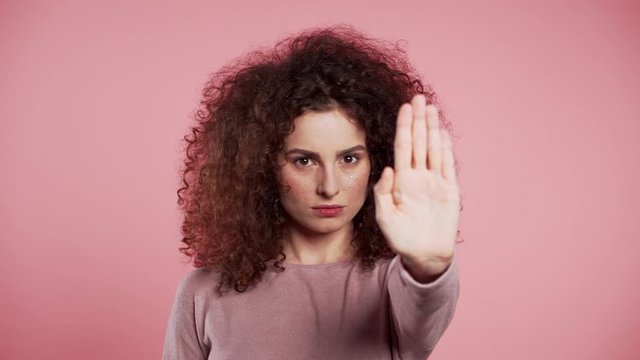 No, never, pretty curly woman disliking and rejecting gesture by stop palm sign. Portrait of young successful confident girl isolated on pink background.