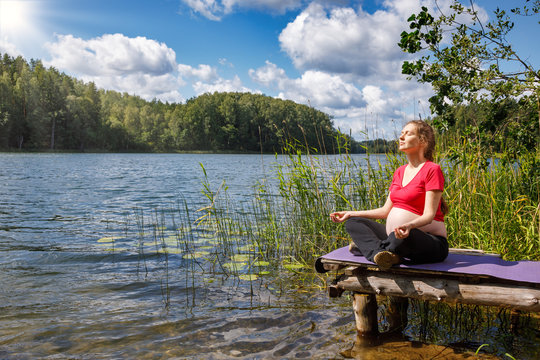 Pregnant woman doing yoga exercise meditating in a summer forest