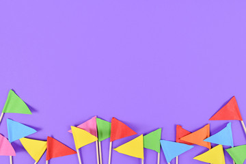 Fototapeta na wymiar Colorful small paper flags at bottom on purple background with copy space