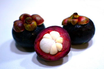 Fresh ripe mangosteen fruits on white table. Cross section showing the thick purple skin and white...