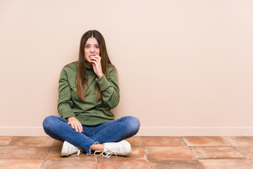 Young caucasian woman sitting on the floor isolated biting fingernails, nervous and very anxious.