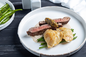 Grilled meat steak New York Striploin. Dumplings with porcini mushrooms in asparagus truffle sauce. On a wooden board on a dark background.