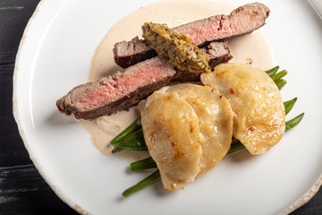 Grilled meat steak New York Striploin. Dumplings with porcini mushrooms in asparagus truffle sauce. On a wooden board on a dark background.