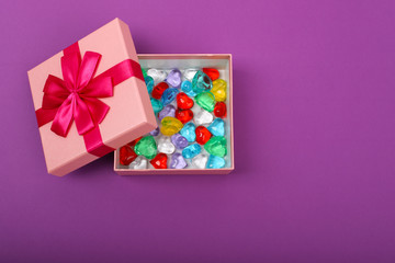 Gift in a pink box on a purple background with copy space. Opened gift box with coloured hearts inside, top view