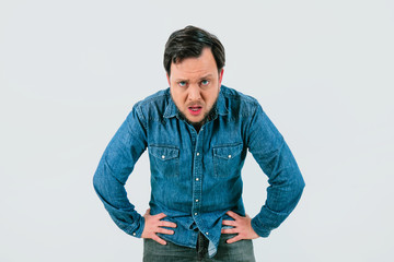 Young man with expression of tiredness and exhaustion. Denim shirt and isolated gray background.