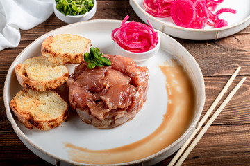 Salt marinated silver carp, diced, next to onion marinated in wine vinegar, fried croutons. Decorated with microgreen. On a wooden background.