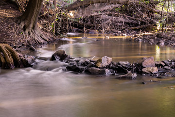 Naklejka na ściany i meble Long exposure picture of a stream flowing with rocks and natural light