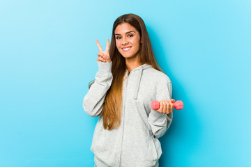 Young fitness woman holding a weight showing victory sign and smiling broadly.