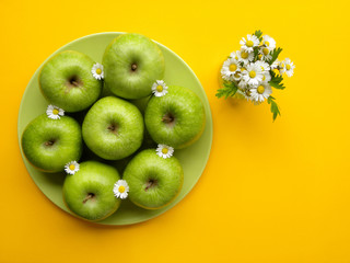 green apples and a bouquet of daisies on a yellow background