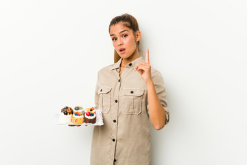 Young caucasian woman holding sweet cakes having an idea, inspiration concept.