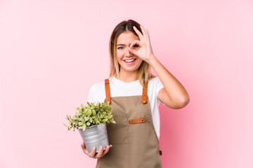 Young caucasian gardener woman in a pink background excited keeping ok gesture on eye.