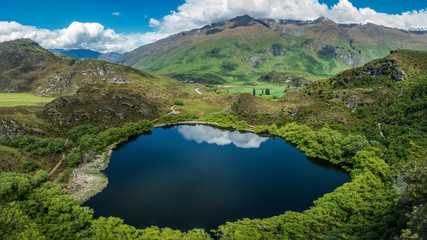 Dark blue pond with green field and hills all around