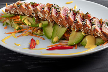 Japanese food. Tataki with tuna. Fried fish with sesame seeds and soy sauce, wasabi, lime. On a pillow of vegetables. Avocados, strips of chili peppers