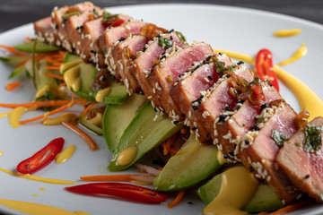 Japanese food. Tataki with tuna. Fried fish with sesame seeds and soy sauce, wasabi, lime. On a pillow of vegetables. Avocados, strips of chili peppers