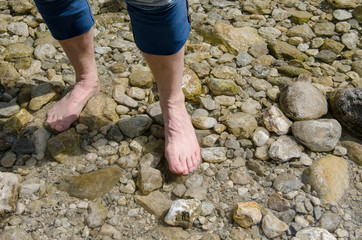 Man walking barefoot on stones with jeans rolled up through clear water