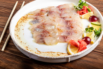 Light-salted dorado with sunflower in truffle oil. Next to slices of lemon, lime, grapes, pickled ginger. To the side of the plate are chopsticks.