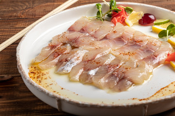 Light-salted dorado with sunflower in truffle oil. Next to slices of lemon, lime, grapes, pickled ginger. To the side of the plate are chopsticks.