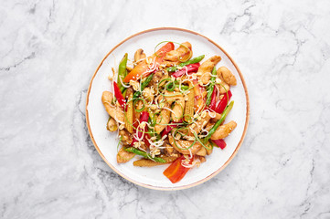 Chicken Chop Suey in white plate on marble background. Chop Suey is American Chinese cuisine dish with different stir fried vegetables, chicken meat and sauces. Copy space. Top view. American food.