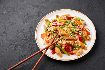 Chicken Chop Suey in white plate at black slate background. Chop Suey is American Chinese cuisine dish with different stir fried vegetables, chicken meat and sauces. Copy space. American food.
