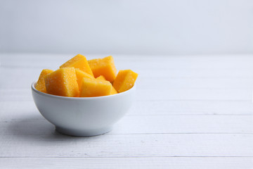 a bowl of mango succades on white wooden background
