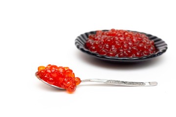 Red Kamchatka caviar lies on a spoon and on a black plate. On a white background