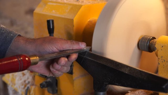 Woodworker handles wood by machine. Builder works with workpiece in workspace. Making authentic handmade plate. Production of wooden trencher. Carpenter cuts wood by gouge in soft focus.